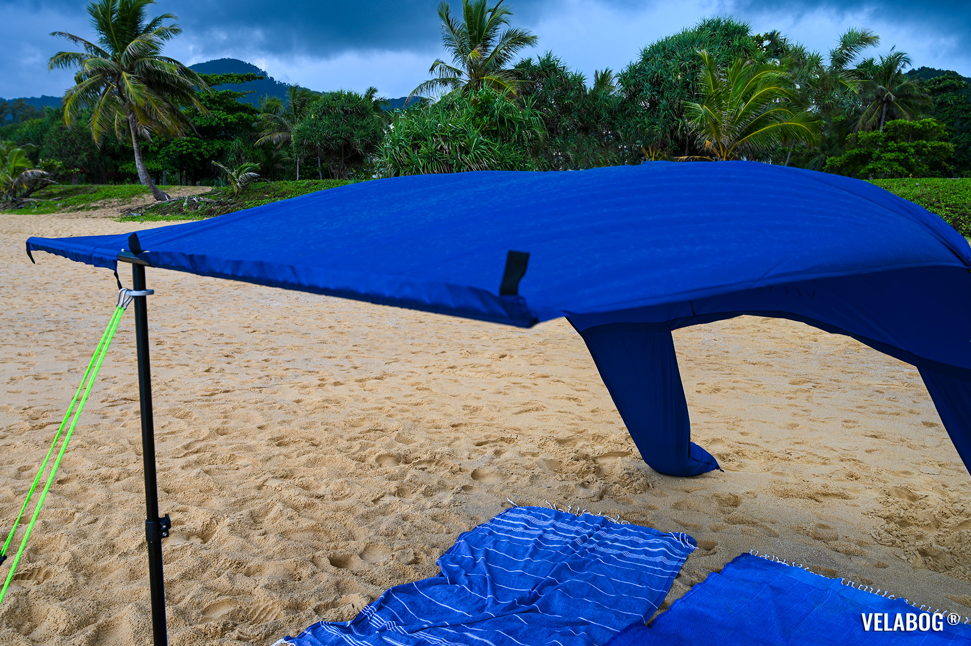 Beach sun sail Velabog Breeze, nightblue on windy rainy beach in Thailand. Best beach canopy tent, best shelter on the beach also by rain. Setup option for light to strong wind. Front view. Details.